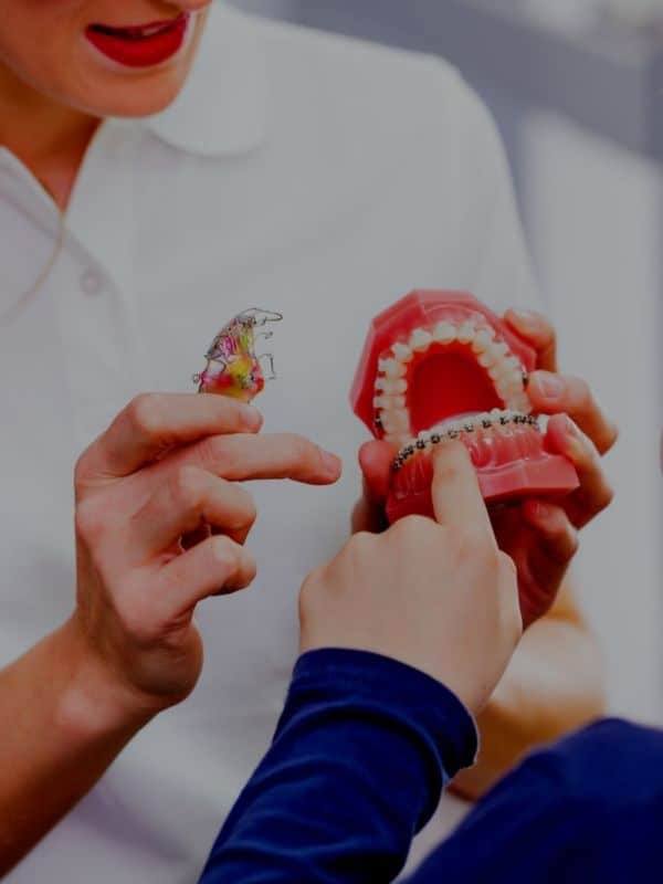 Orthodontist showing patient a model smile with metal braces