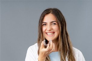 Woman in white shirt holding Invisalign aligner