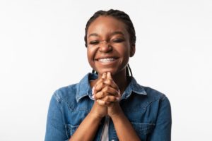 Woman with braces smiling with hands clasped together