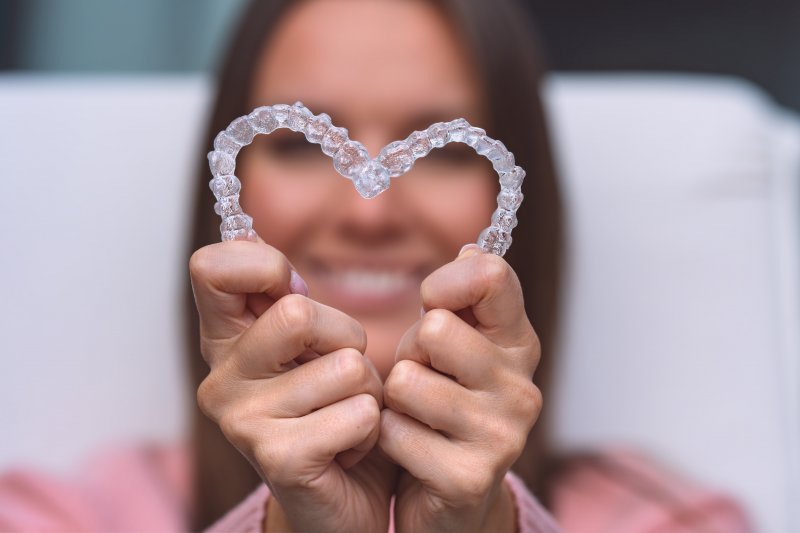 A woman holding two Invisalign aligners in the shape of a heart.