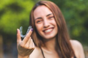 Woman smiling while holding up her clear aligner